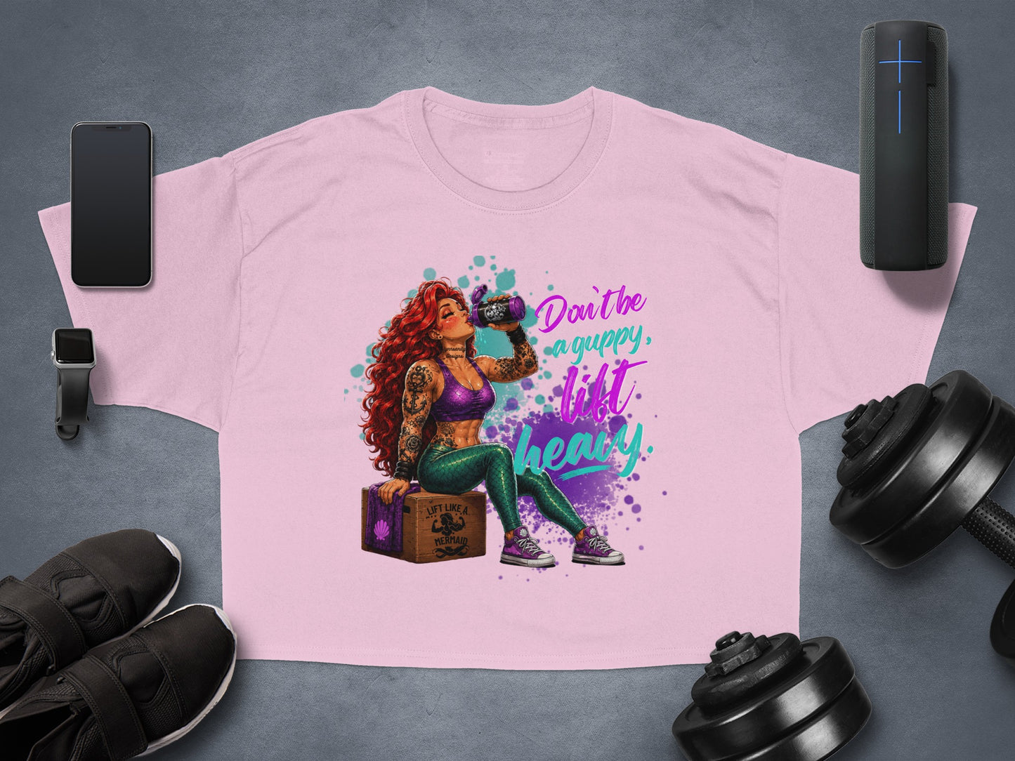 Pink graphic t-shirt with mermaid lifting weights, saying "Don't be a guppy, lift like a mermaid."