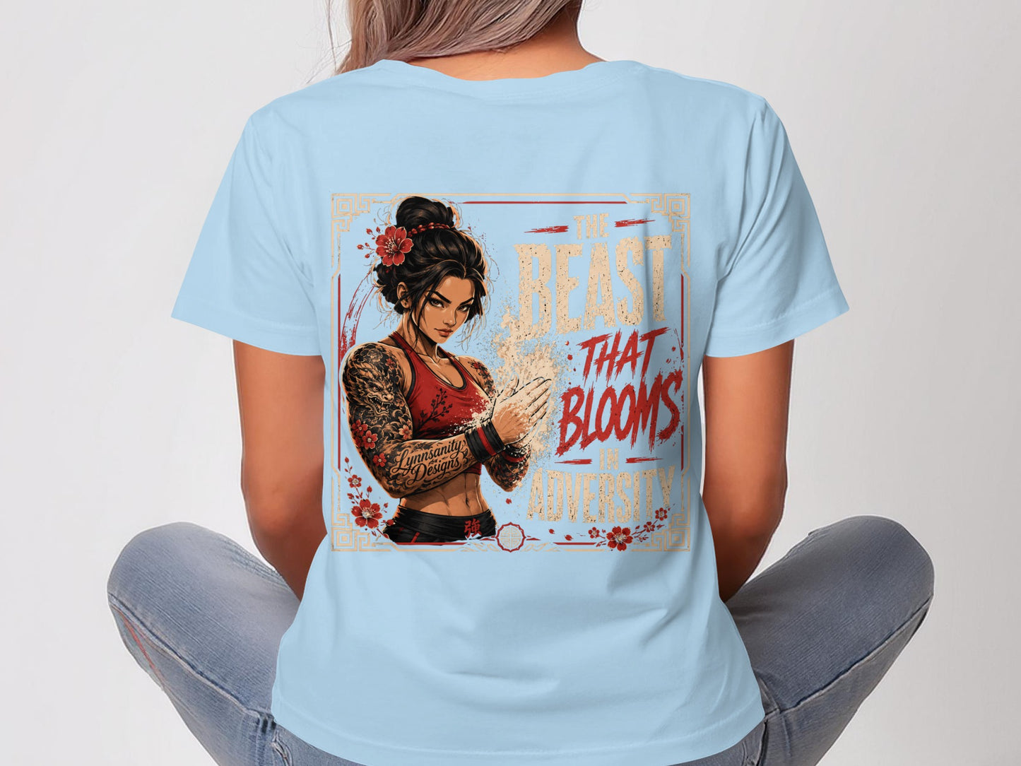 Woman in light blue t-shirt with graphic of a woman with tattoos, chest binder, and flower in hair.