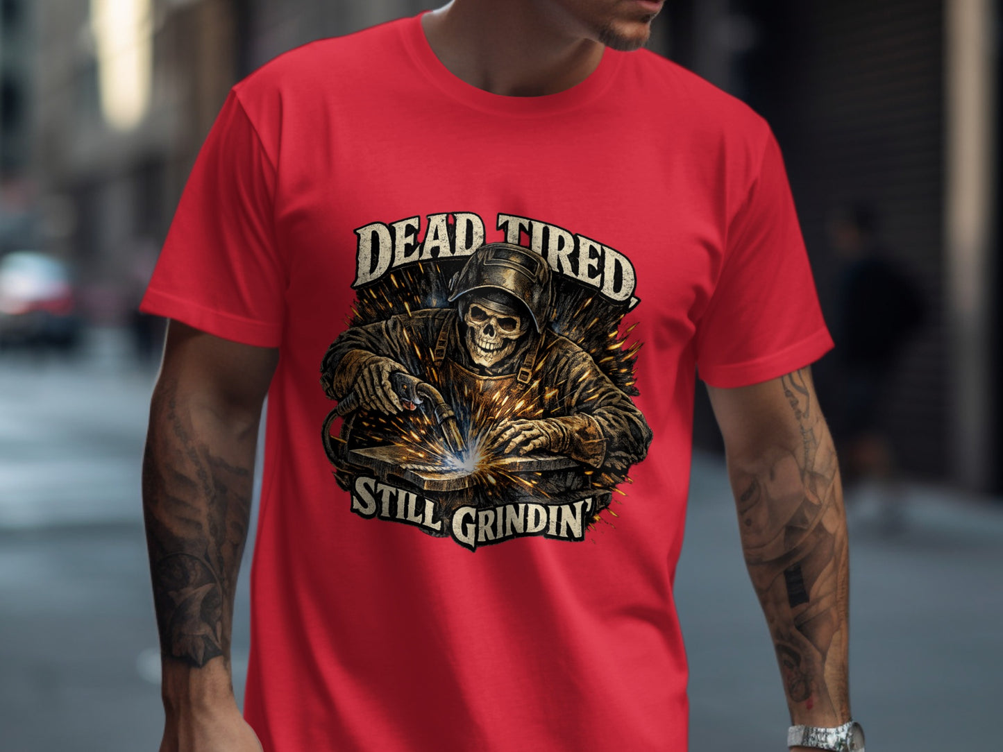 Red t-shirt featuring a skull welding with "DEAD TIRED STILL GRINDIN'" text.