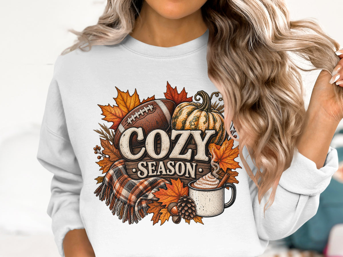 Autumn graphic on white sweatshirt featuring football, pumpkin, hot drink, and text "Cozy Season".