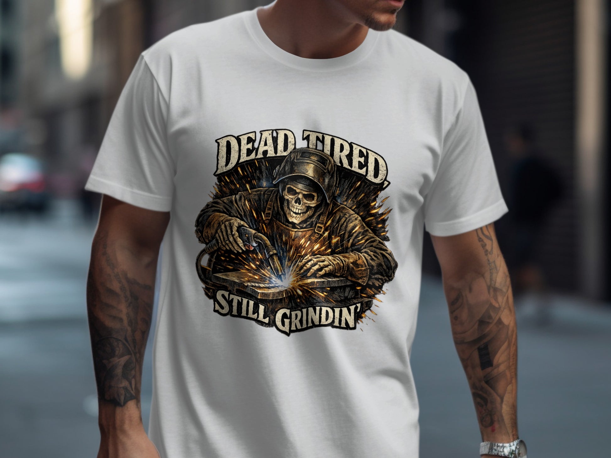 Welder wearing a mask, sparks flying, text reads "DEAD TIRED STILL GRINDIN".