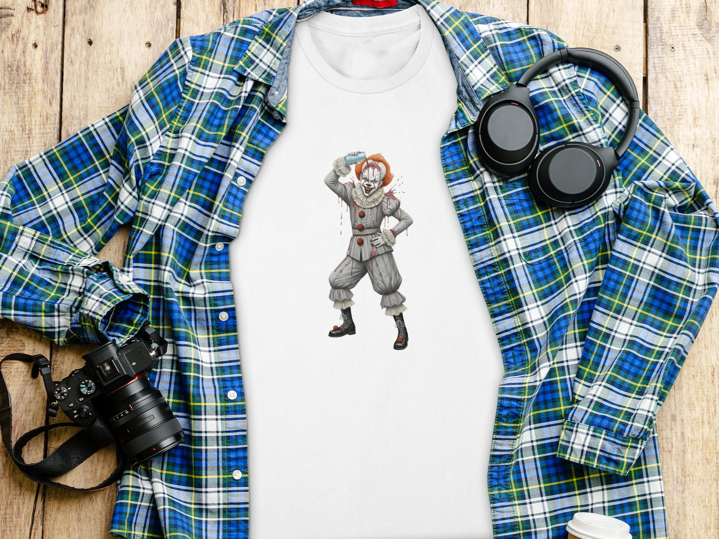 White t-shirt with Pennywise clown illustration, laid flat with plaid shirt and headphones.