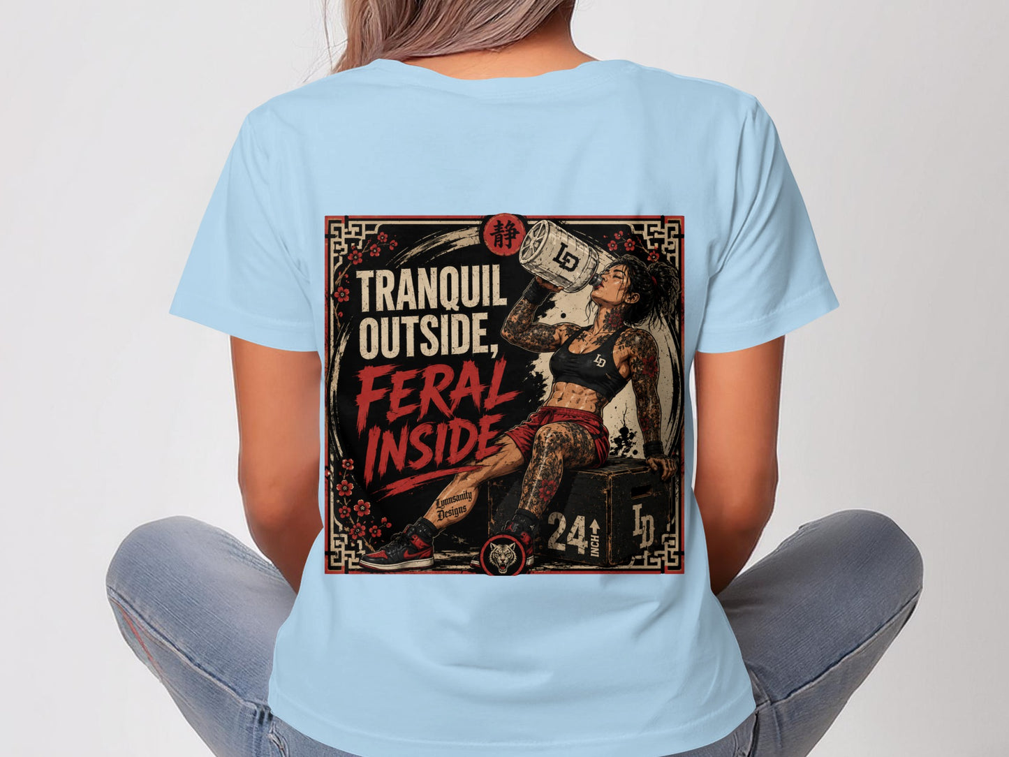 Woman wearing light blue t-shirt with "Tranquil Outside, Feral Inside" graphic.
