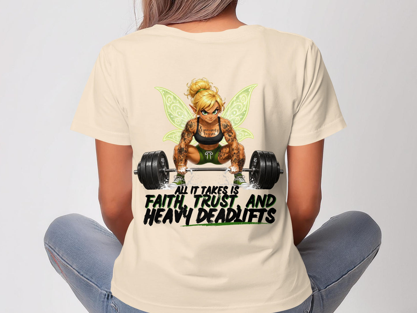 Woman wearing a shirt with a muscular fairy and "All it takes is faith, trust, and heavy deadlifts" text.
