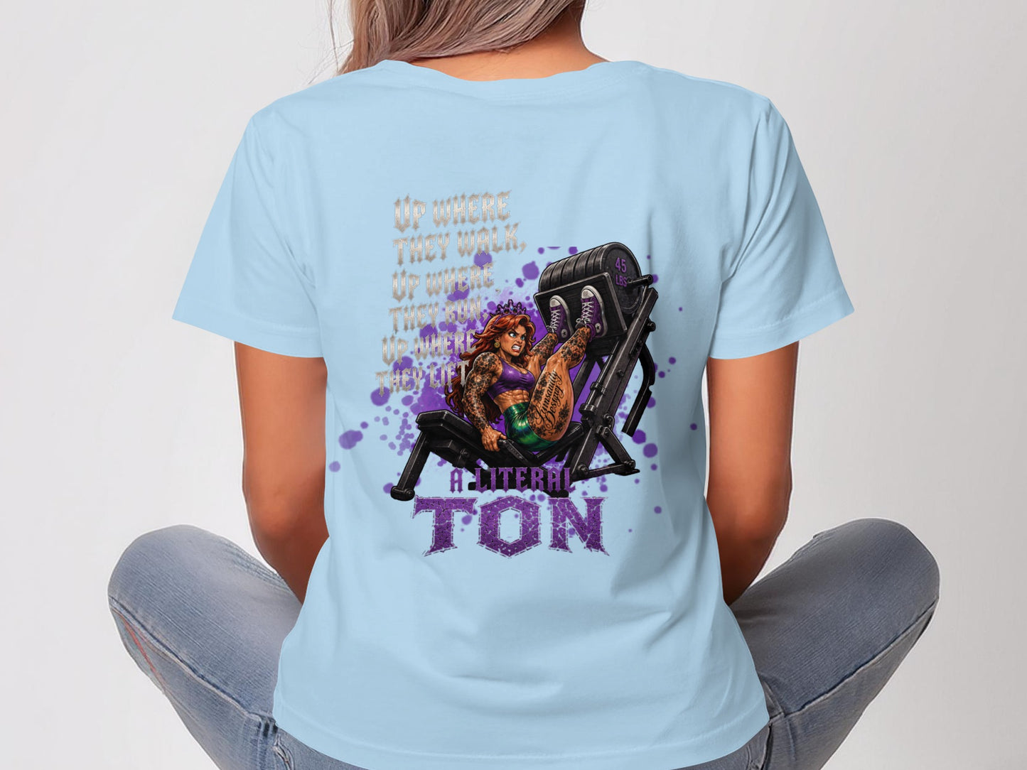 Woman in light blue t-shirt with graphic of woman on leg press machine.