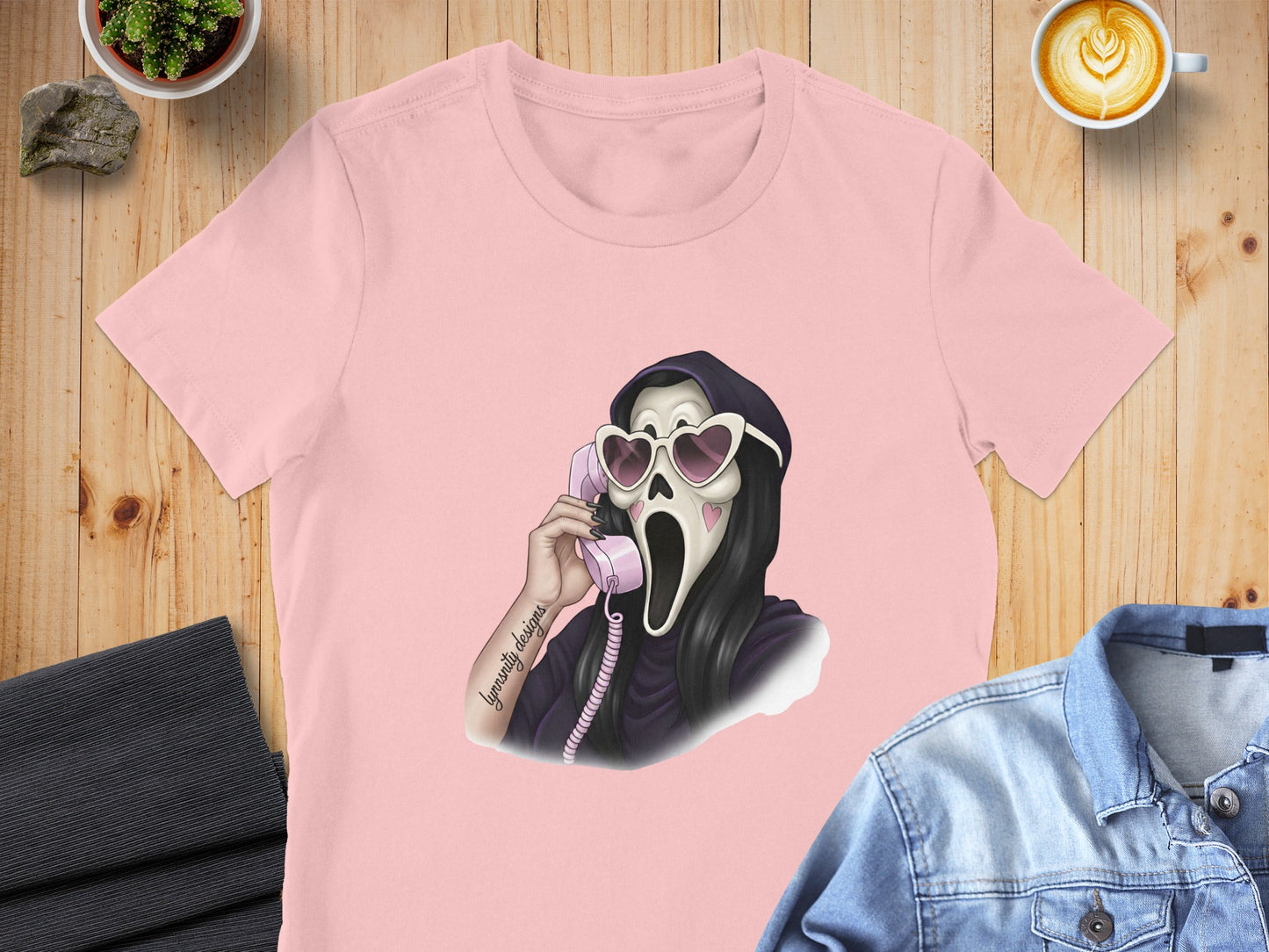 Pink t-shirt with a graphic of a skull in heart sunglasses talking on a pink phone.