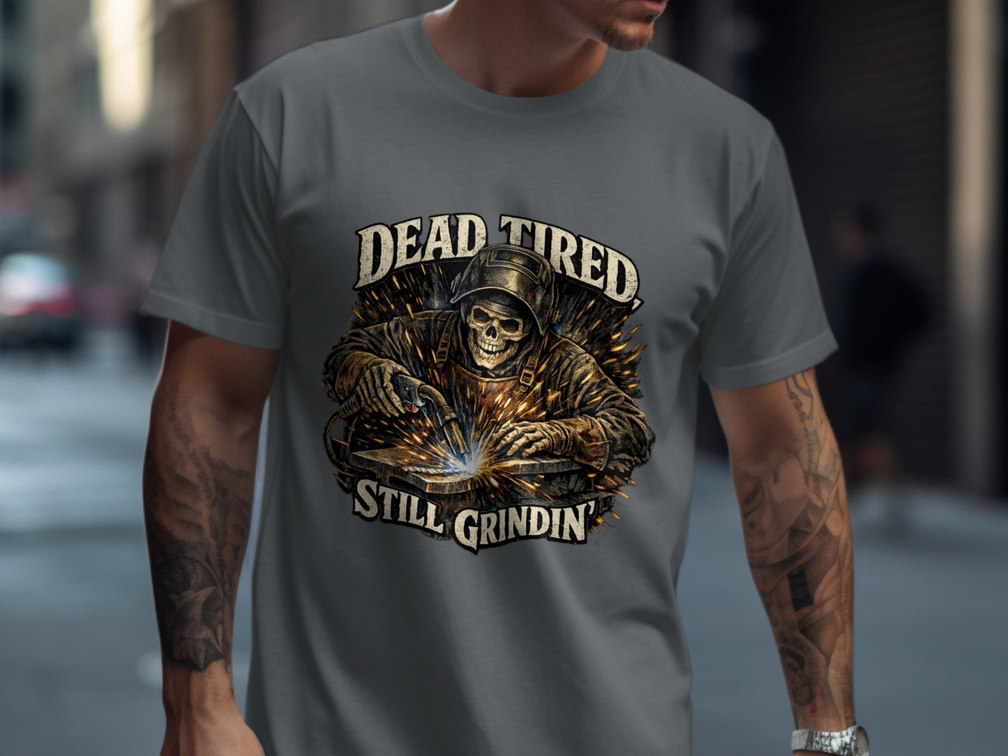 T-shirt graphic with skull welder and text "Dead Tired Still Grindin'".