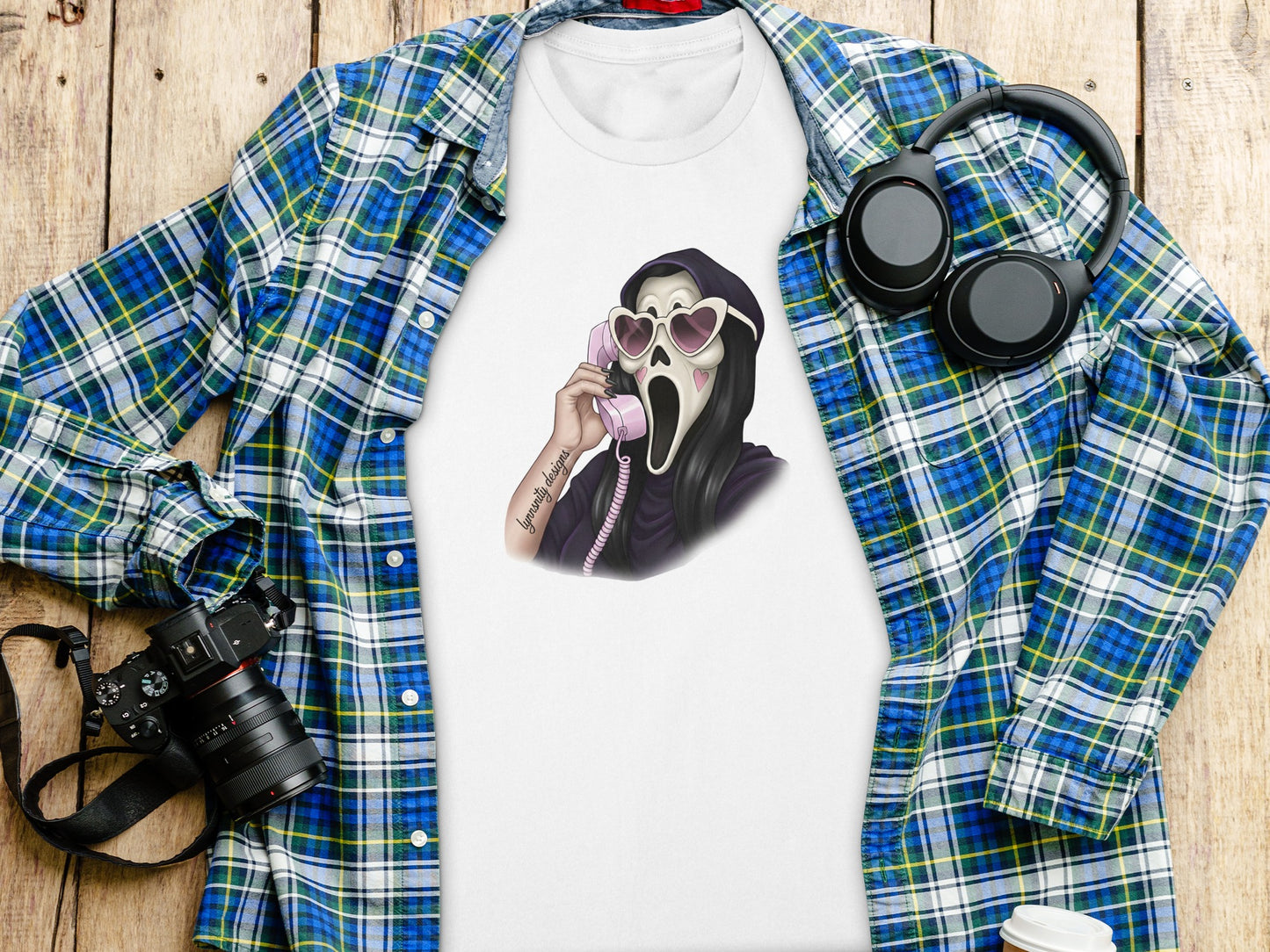 White t-shirt with ghost face graphic wearing heart sunglasses talking on pink phone.