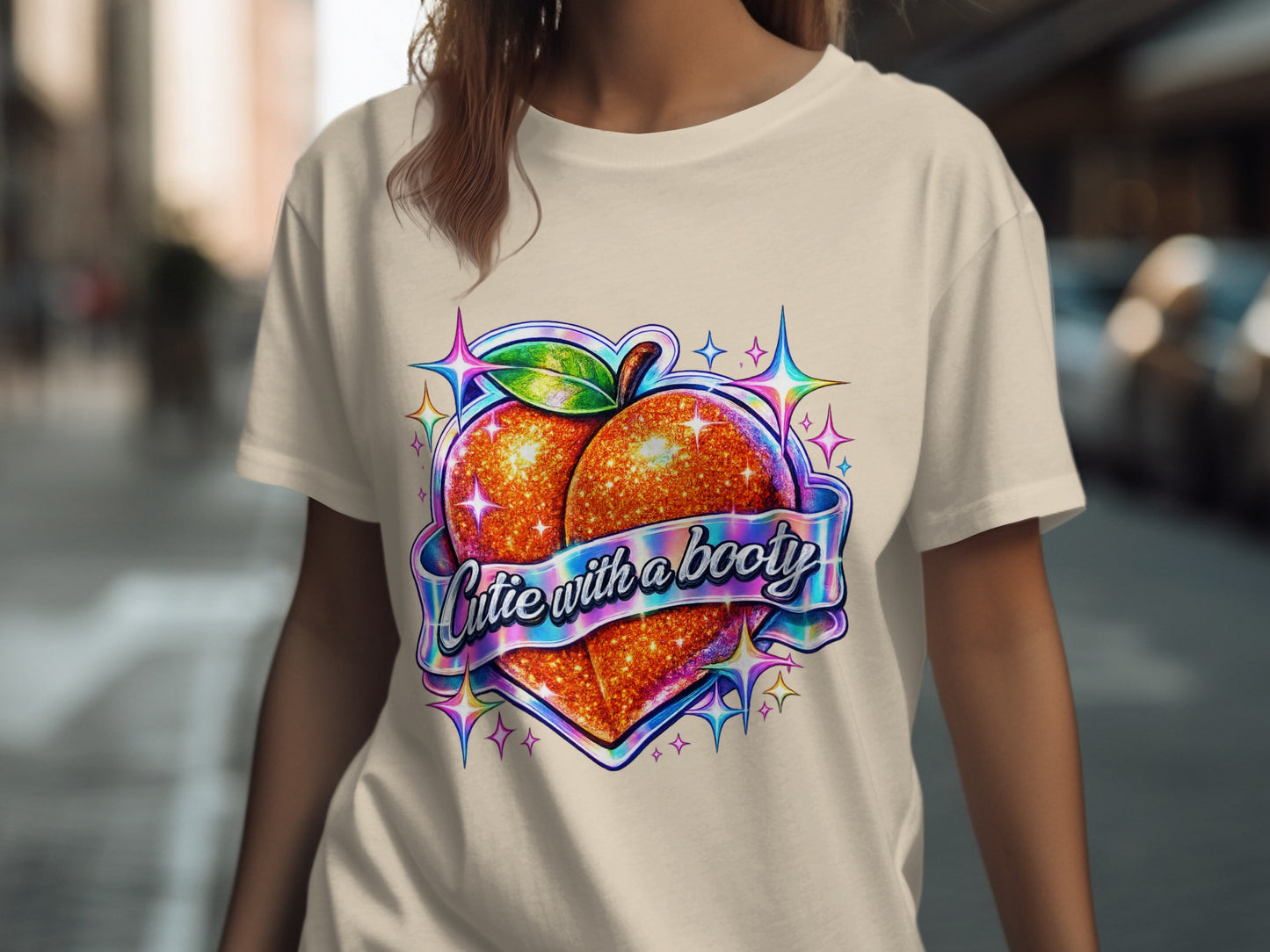 Peach graphic with glitter effect and "cutie with a booty" text on a beige t-shirt.