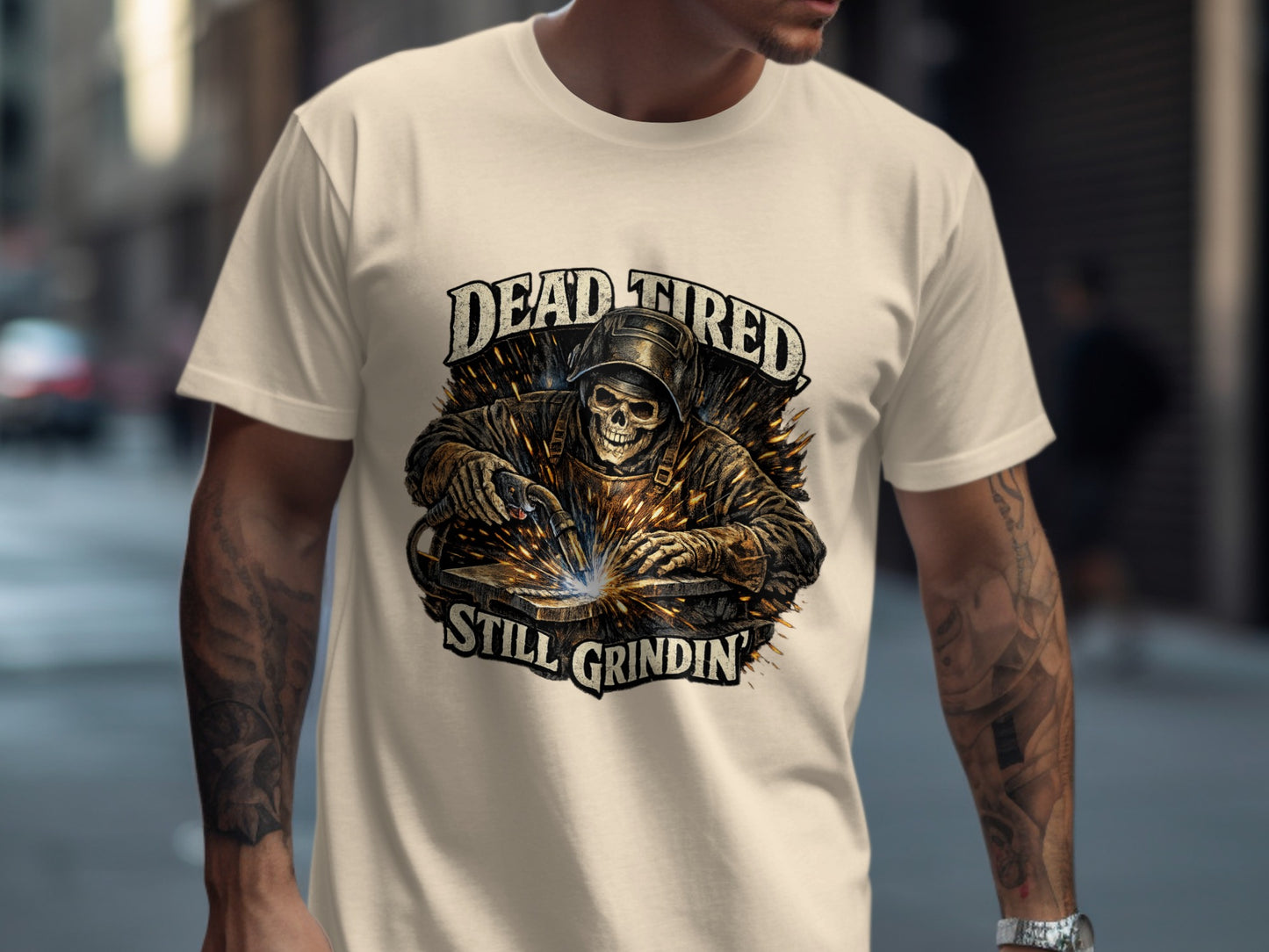T-shirt with graphic of a welder and text "DEAD TIRED STILL GRINDIN".