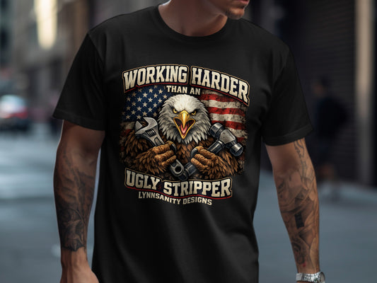 Black t-shirt with an eagle holding tools and the text "Working Harder Than an Ugly Stripper".