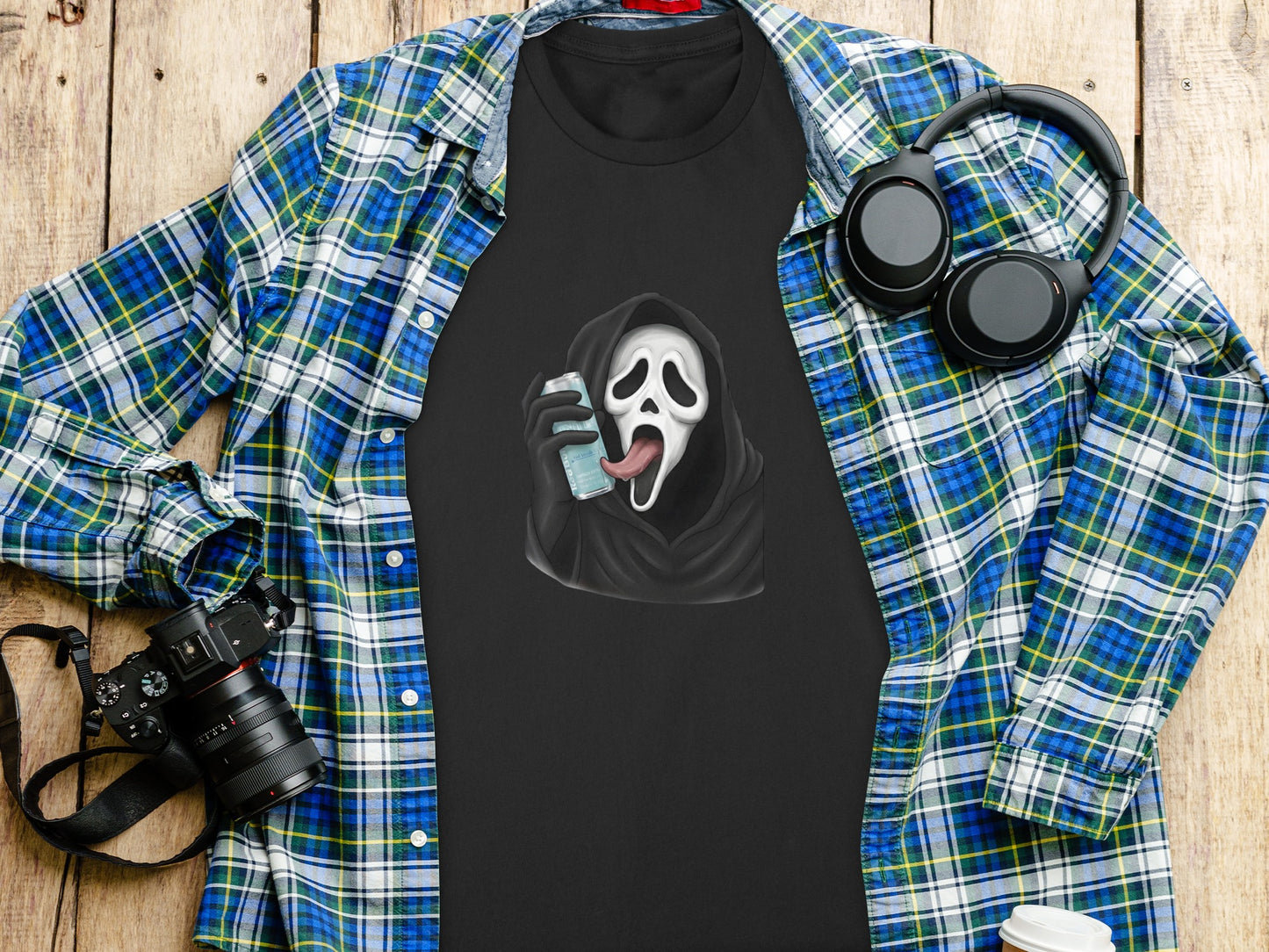 Black t-shirt with Ghostface holding a phone, laid on a flannel shirt and wooden background.