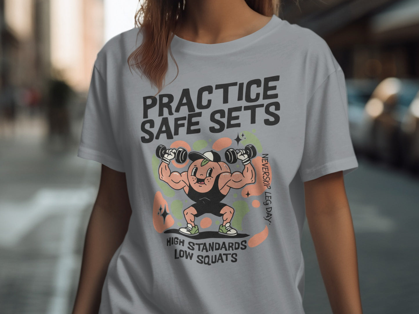 Graphic tee with cartoon of muscular figure lifting weights, text "Practice Safe Sets".