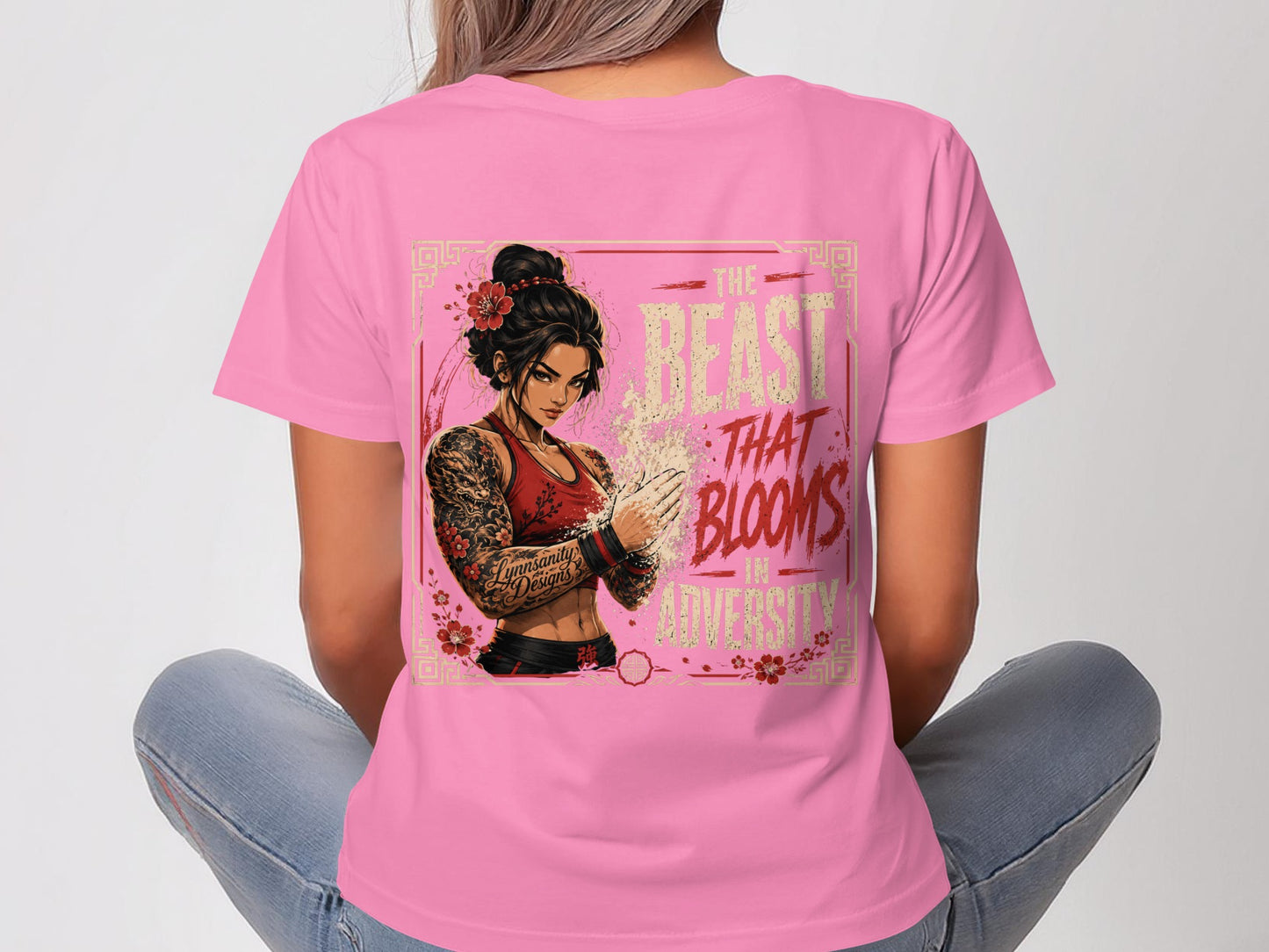 Pink t-shirt with tattooed woman flexing, text reads "The Beast That Blooms In Adversity".