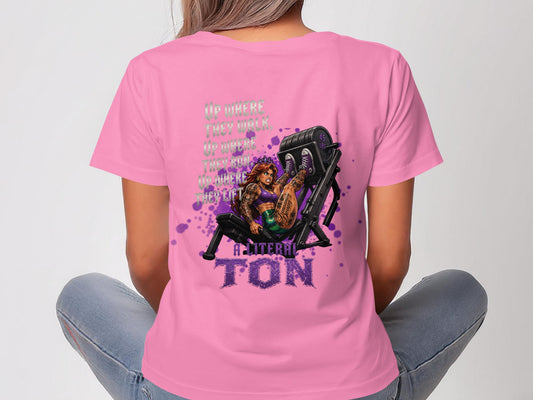 Woman in pink shirt with back graphic of a tattooed woman on a weight machine.