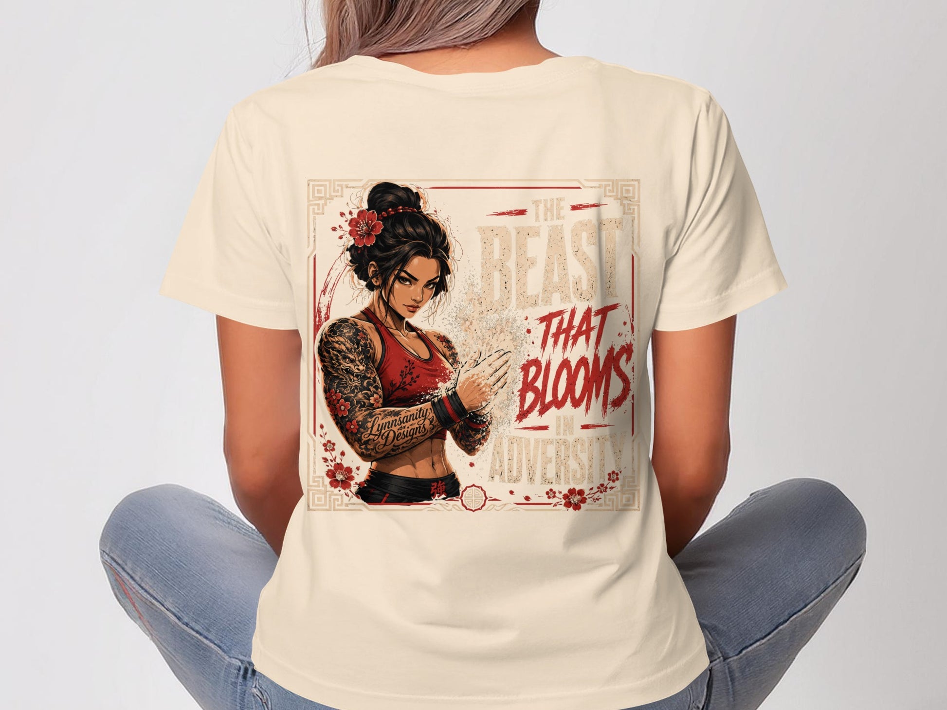 Woman wearing a cream t-shirt with a design of a tattooed woman and "The Beast That Blooms in Adversity" text.